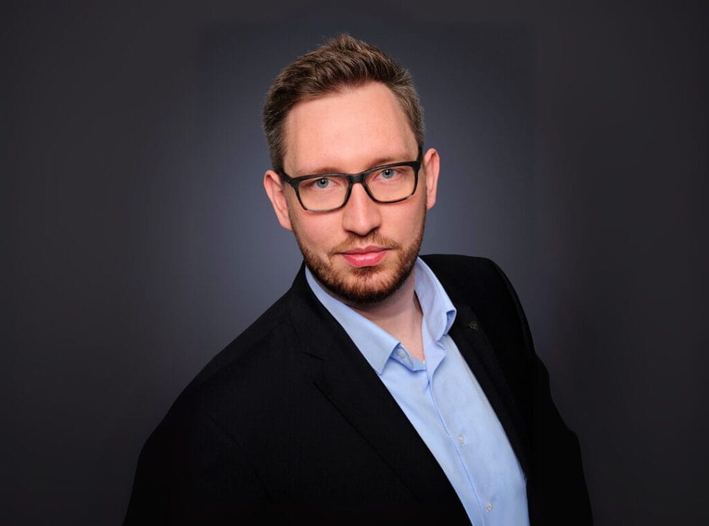 Mann mit Brille im Anzug vor grauem Hintergrund